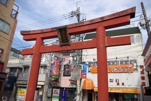 駅前の鳥居をくぐると下町風景の商店街。環八の先には異質な空港・物流関係の大きな建物。