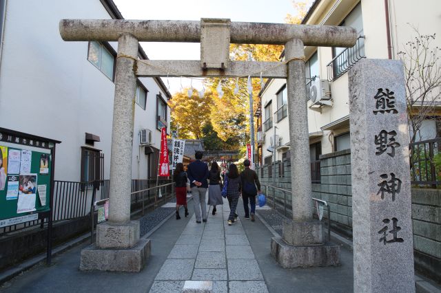 東側より、建物の間に鳥居があります。参拝者が次々と出入りします。