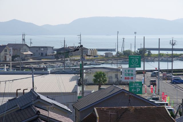 ダイソー等チェーン店が集まる地区、停泊するボート、海、山並の風景。