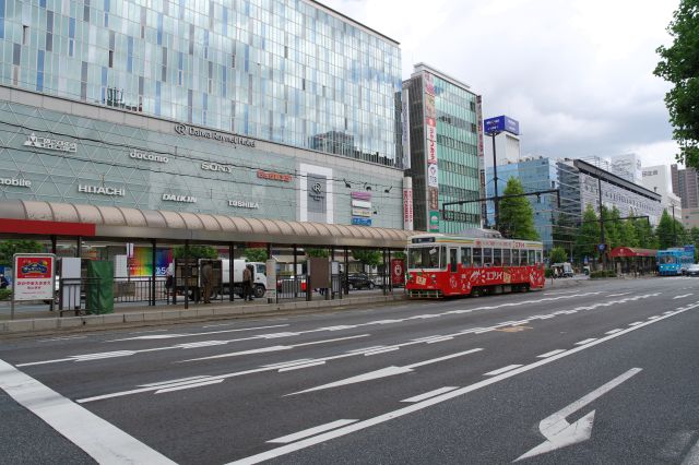 ビルが囲う駅前の大通りを行き交う路面電車。